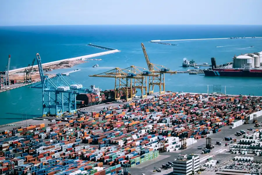 Aerial view of a container terminal with rows of stacked containers, gantry cranes, and a docked ship