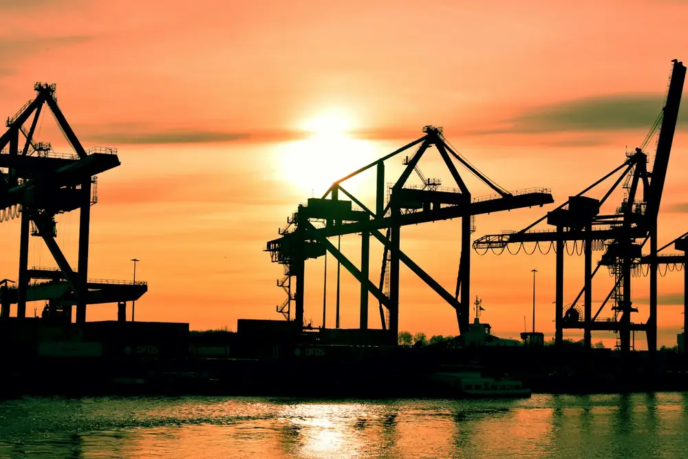 Gantry cranes silhouetted against a sunset sky at a container terminal