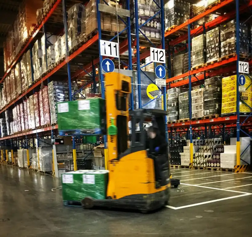 Reach truck carrying a wrapped pallet down a warehouse aisle between tall pallet racks