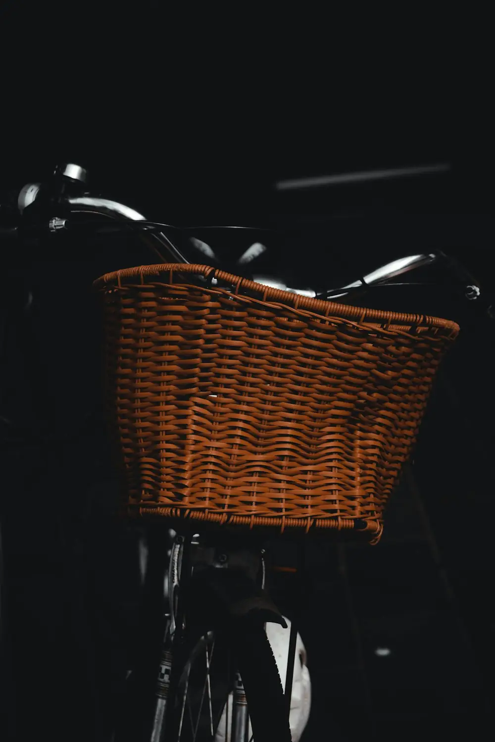 Close-up of a wicker basket and chrome handlebars on a bicycle in low light