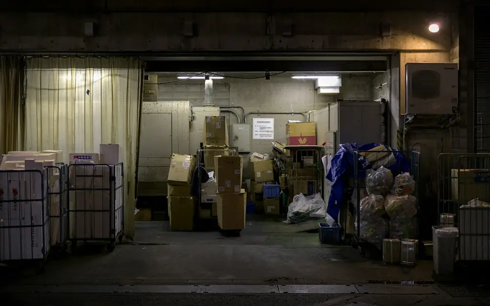 Roll cages and stacked boxes inside a dimly lit depot loading bay at night
