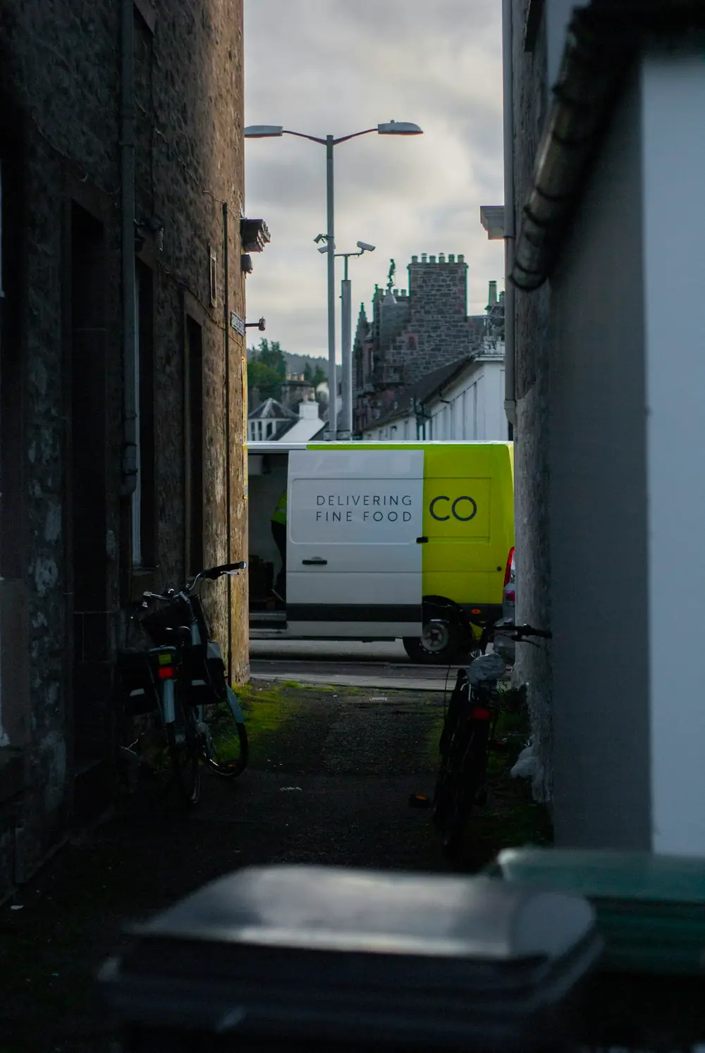 A delivery van parked at the end of a narrow stone alley with bicycles leaning against the walls